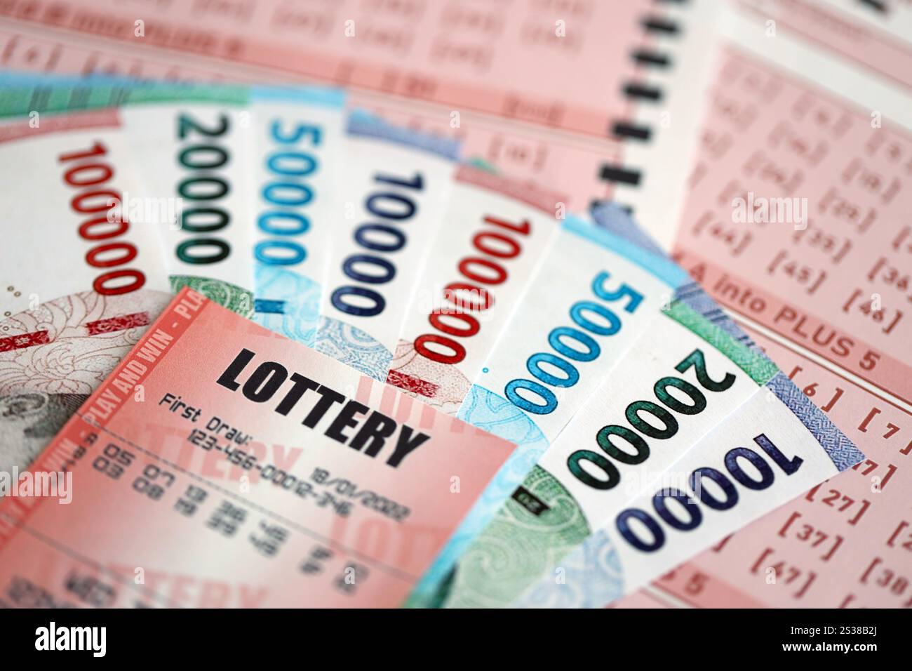 Billet de loterie rouge se trouve sur des feuilles de jeu roses avec des factures d'argent rupiah indonésiennes. Concept de jeu de loterie ou dépendance au jeu en indonésie. Rouge Banque D'Images