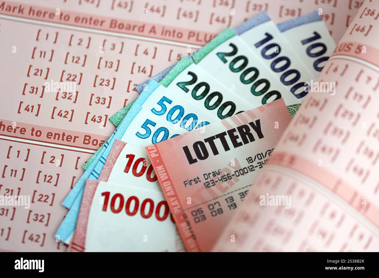 Billet de loterie rouge se trouve sur des feuilles de jeu roses avec des factures d'argent rupiah indonésiennes. Concept de jeu de loterie ou dépendance au jeu en indonésie. Rouge Banque D'Images