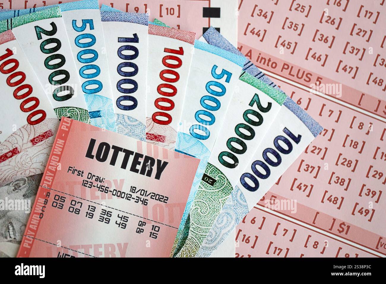 Billet de loterie rouge se trouve sur des feuilles de jeu roses avec des factures d'argent rupiah indonésiennes. Concept de jeu de loterie ou dépendance au jeu en indonésie. Rouge Banque D'Images