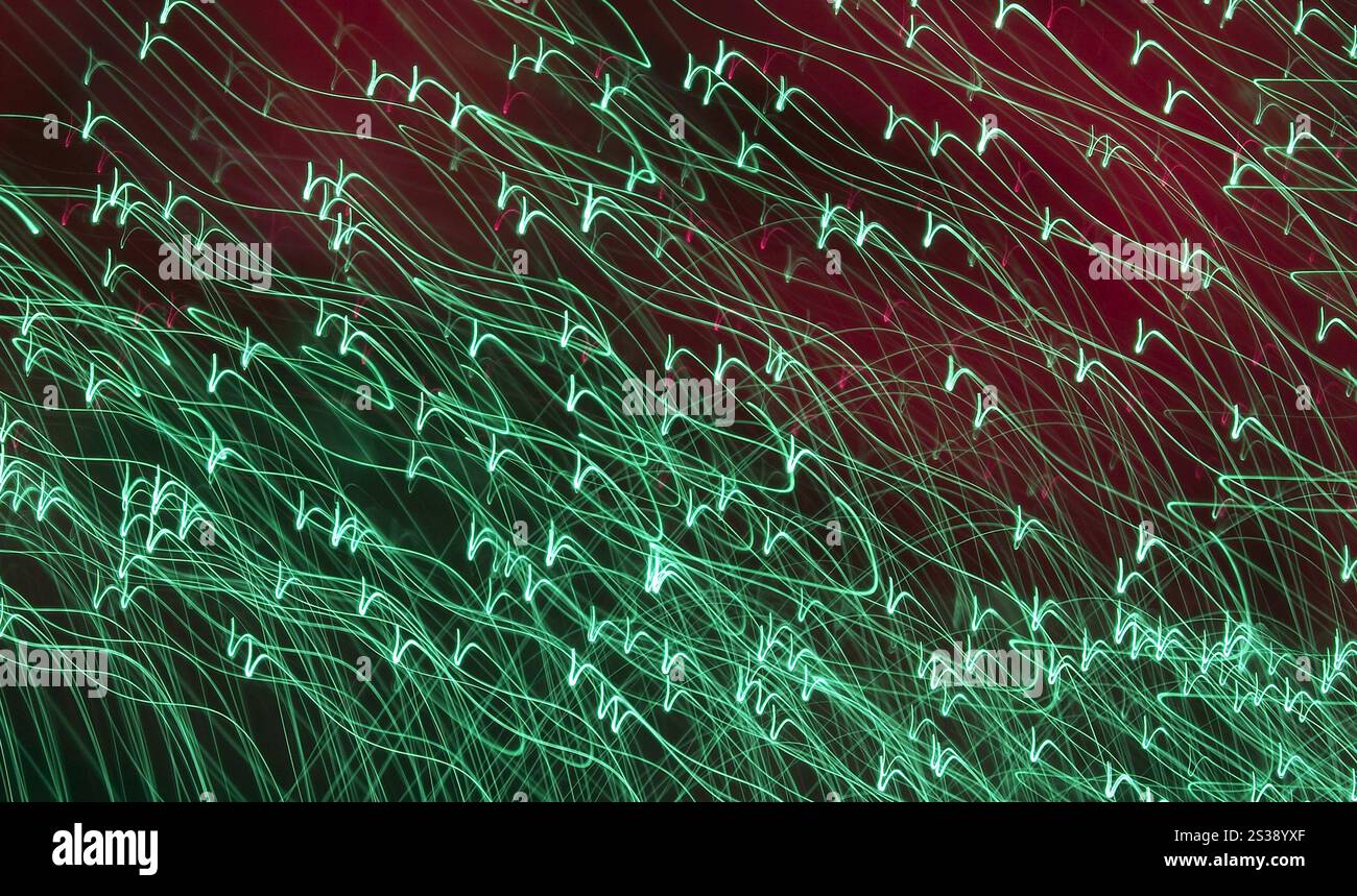 Des stries de lumière verte et blanche entrelacées créent un motif abstrait dynamique sur un fond rouge foncé. Traînées de lumière abstraites sur fond sombre Banque D'Images