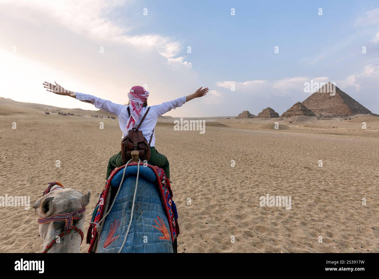 Chameaux dans le complexe de la pyramide de Gizeh - Une femme avec un turban rouge et les bras en montant un chameau à travers de minces dunes de sable - le Caire, Egypte Banque D'Images