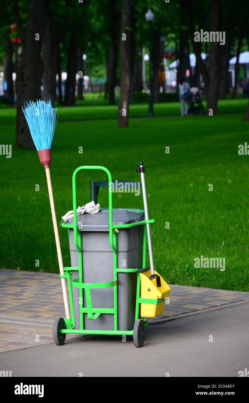 Chariot de service de nettoyage plein de fournitures et d'équipement avec poubelle grise pour un nettoyant professionnel contre l'herbe verte dans le parc public. Nettoyage Banque D'Images