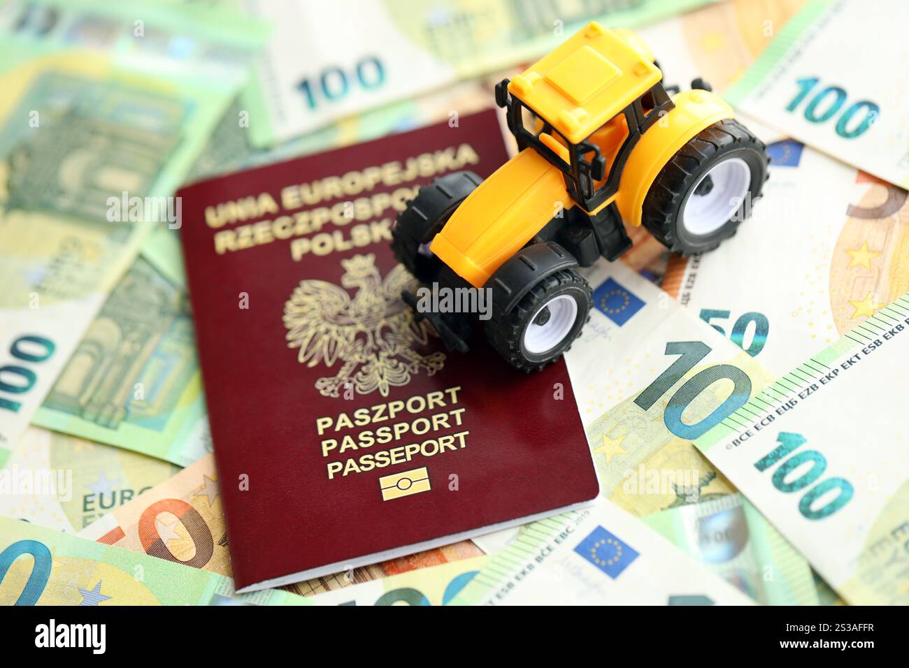 Passeport polonais rouge et tracteur jaune sur les billets d'argent en euros gros plan. Passeport polonais rouge et tracteur jaune sur les billets d'argent en euros Banque D'Images