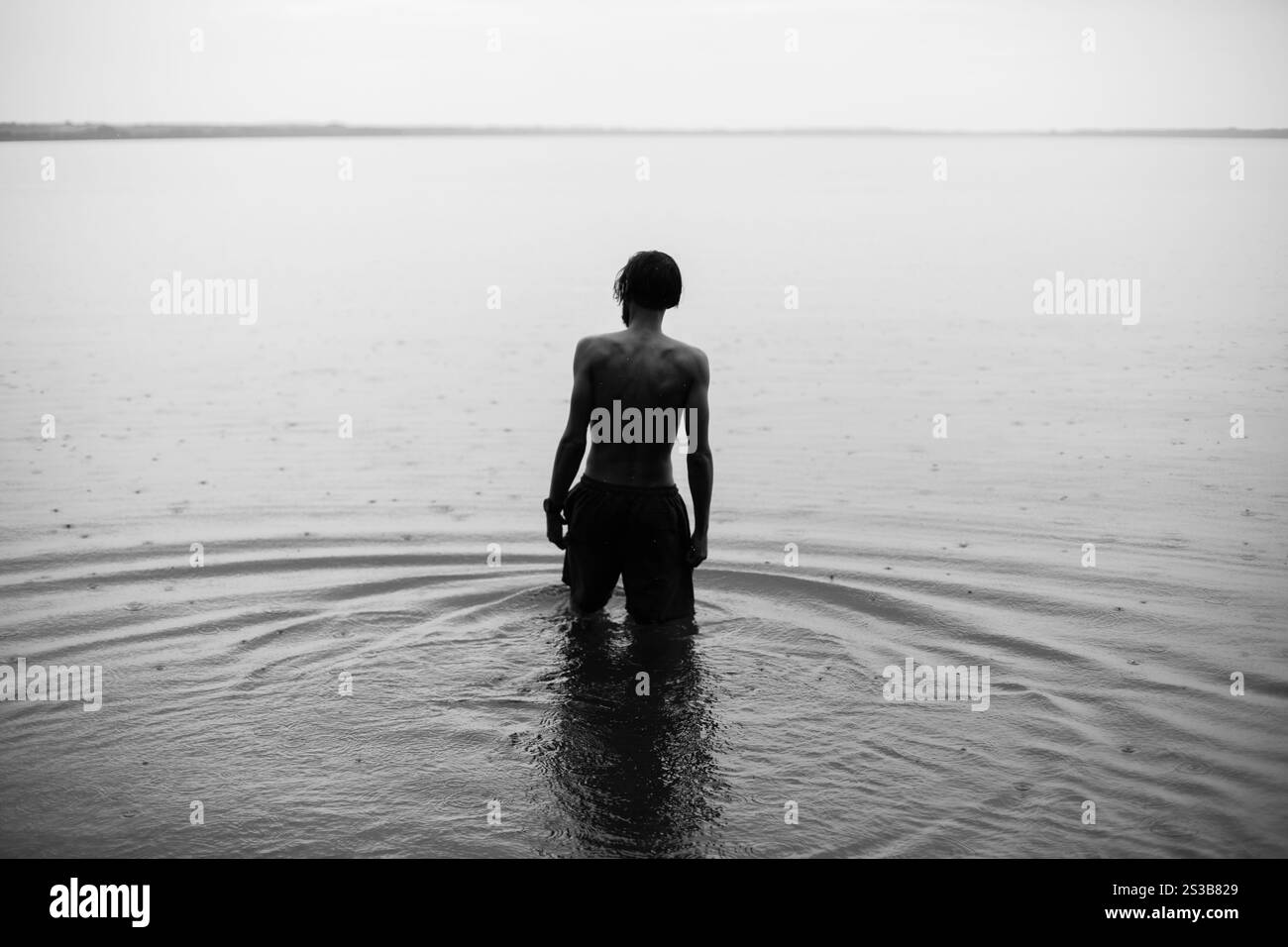 Mince jeune homme marchant dans l'eau quand la pluie tombe dans le lac Banque D'Images