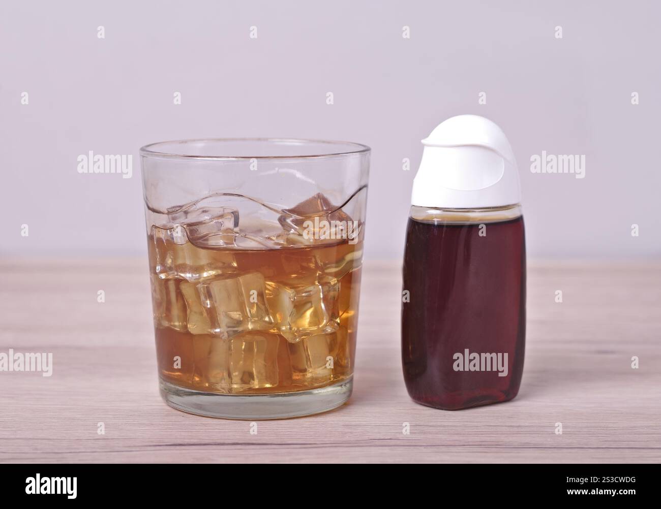 Boire avec des glaçons à côté de la bouteille de concentré de sirop. Banque D'Images