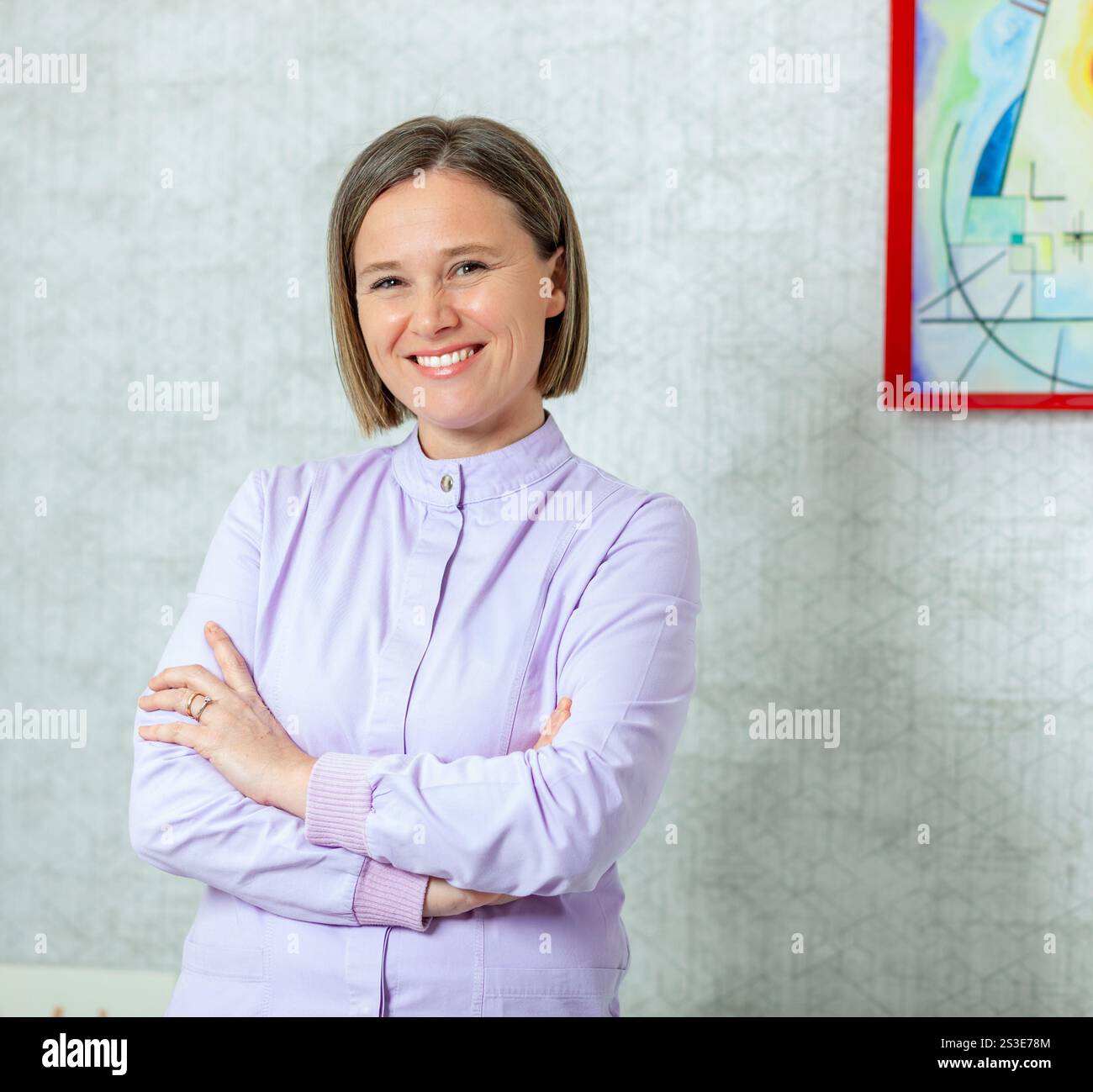 Dentiste féminine confiante souriant avec les bras croisés, mettant en valeur le professionnalisme et l'expertise dans un cadre de clinique dentaire Banque D'Images