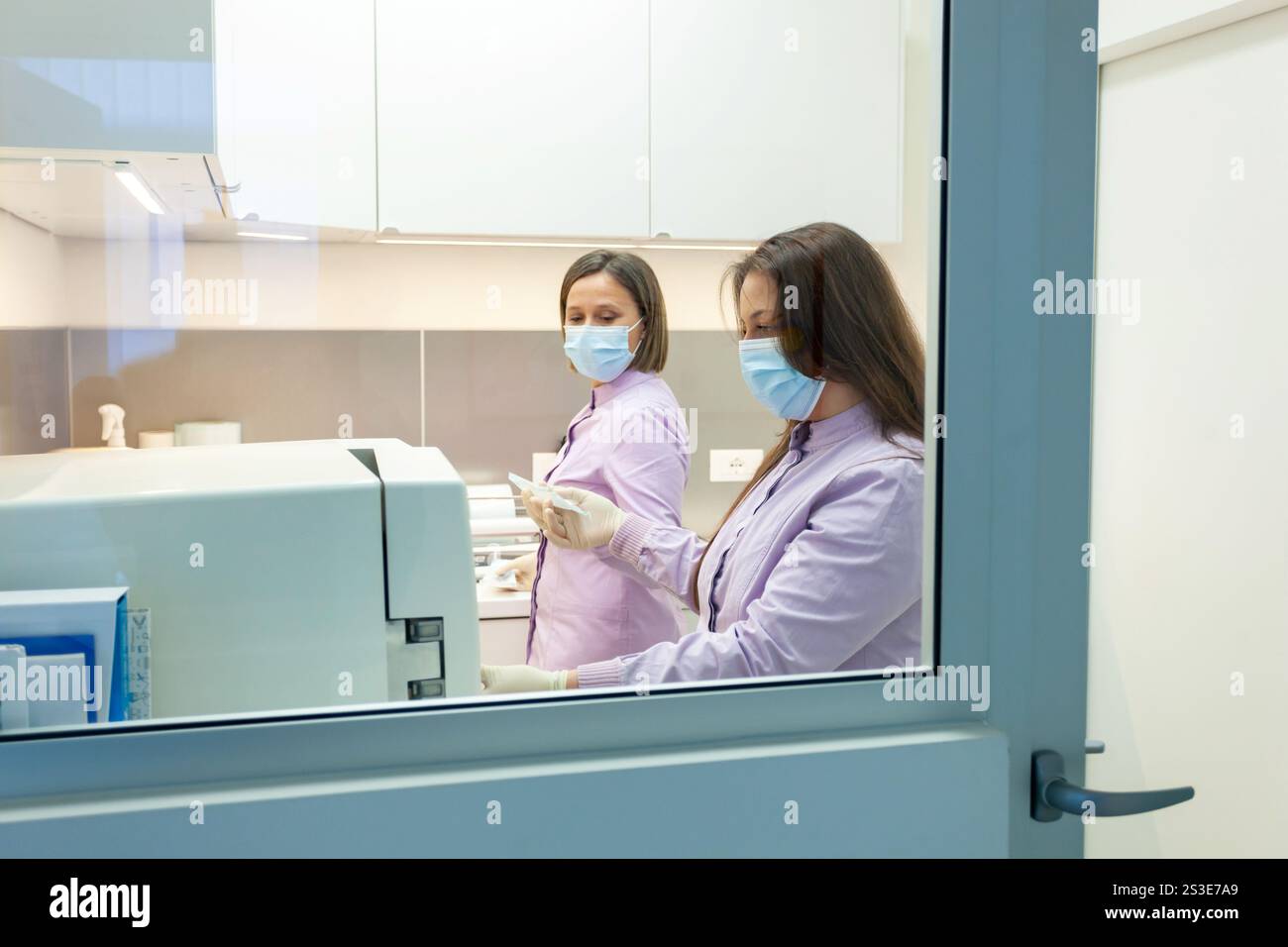 Deux dentistes travaillent avec un stérilisateur autoclave dans une clinique dentaire, portant des masques chirurgicaux et des gants, assurant l'hygiène et la sécurité Banque D'Images