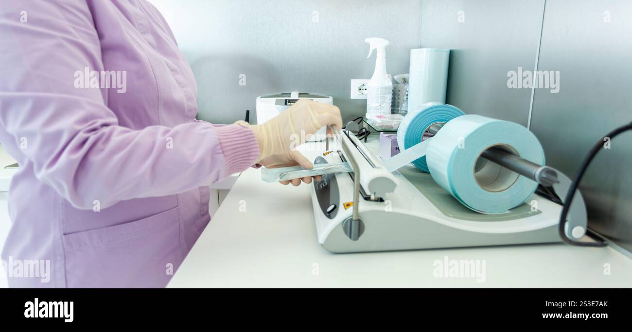 Infirmière portant des gants emballant des instruments médicaux à l'aide d'une machine d'emballage sous vide dans une clinique dentaire Banque D'Images