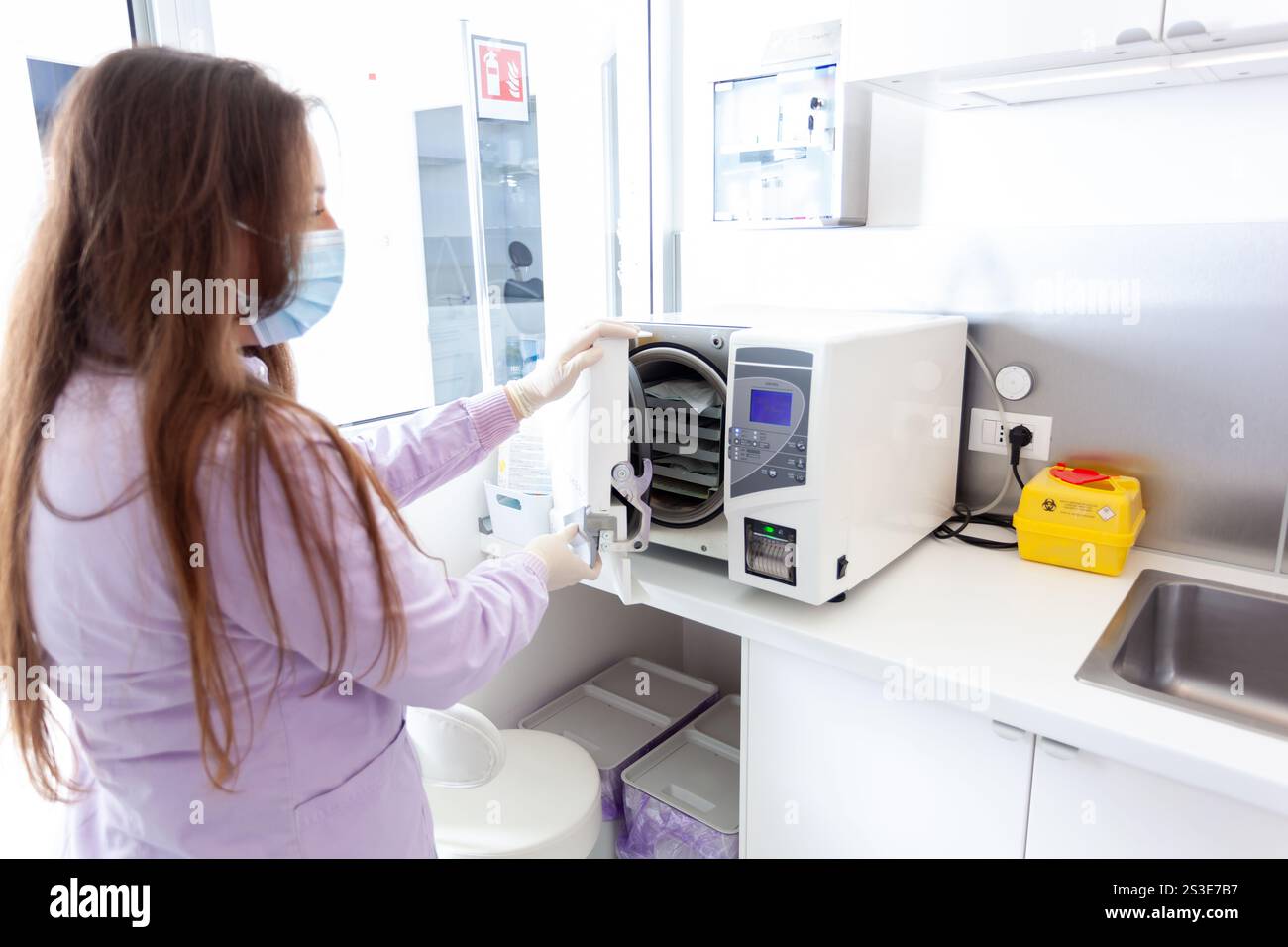 Infirmière portant un masque et des gants en autoclave pour stériliser les instruments médicaux dans une clinique moderne Banque D'Images