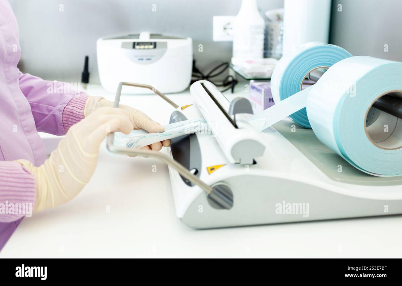 Infirmière portant des gants emballant des instruments dentaires stérilisés à l'aide d'une machine à sceller en clinique dentaire Banque D'Images