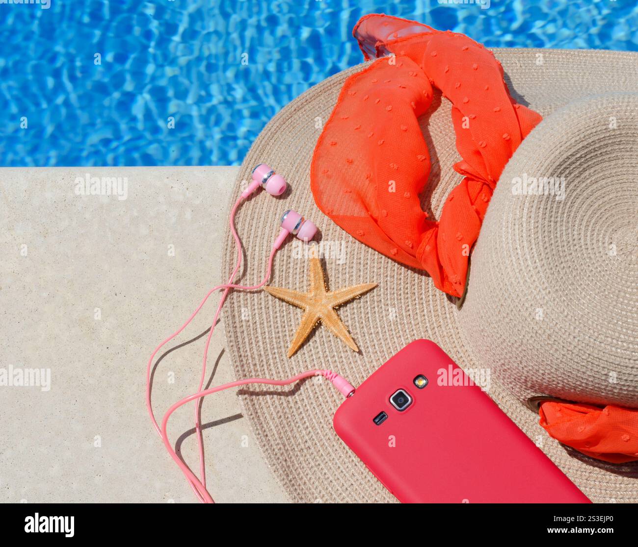 Chapeau de raphia pour femmes, téléphone et étoile de mer à côté de la piscine sur fond d'eau bleue. Banque D'Images