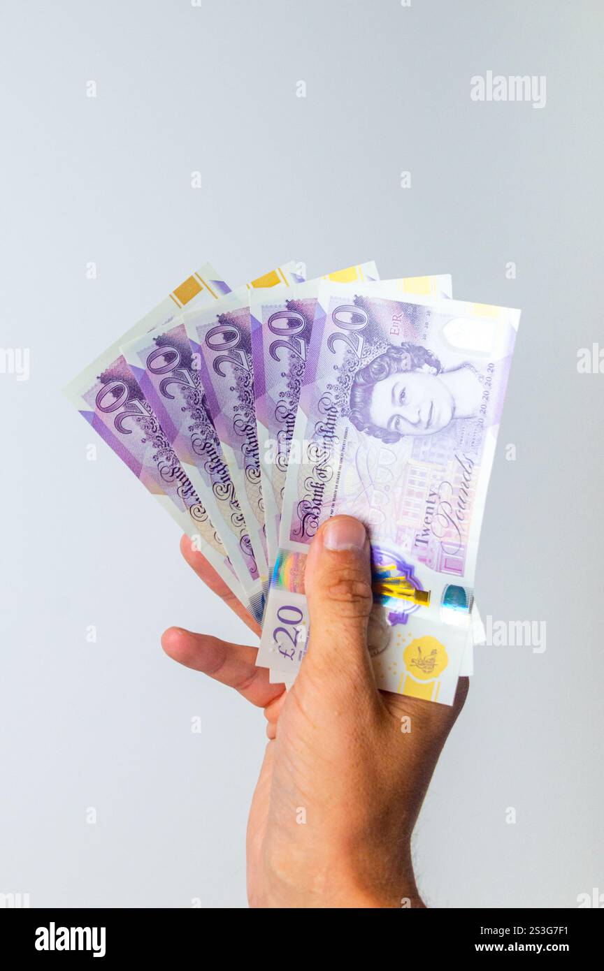 5 billets de vingt livres sterling tenus dans sa main droite. Banque D'Images