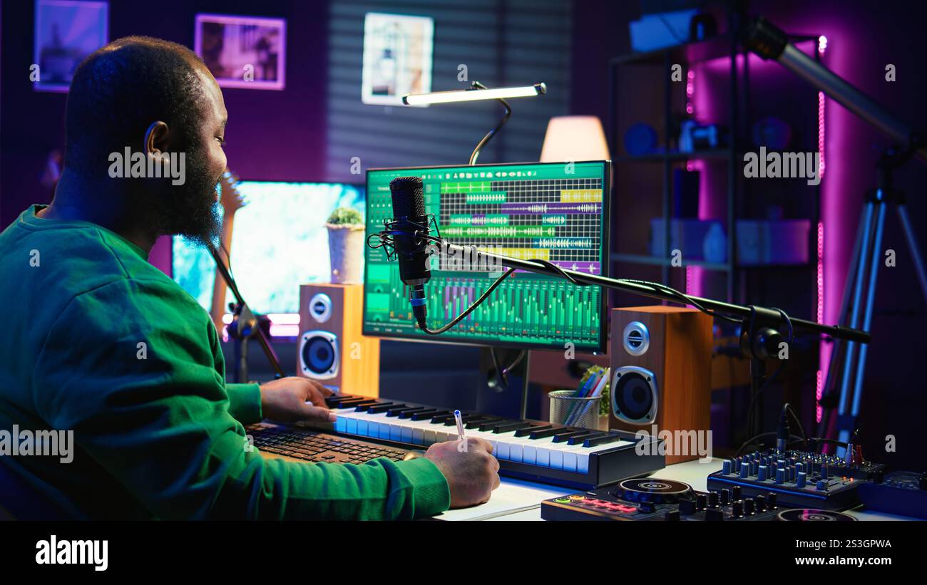 Auteur-compositeur prenant des notes pour créer de nouvelles pistes pour un album dans son home studio, écrivant des paroles et des éléments harmoniques avant d'enregistrer sa chanson et montage sur logiciel, ingénierie acoustique. Caméra B. Banque D'Images