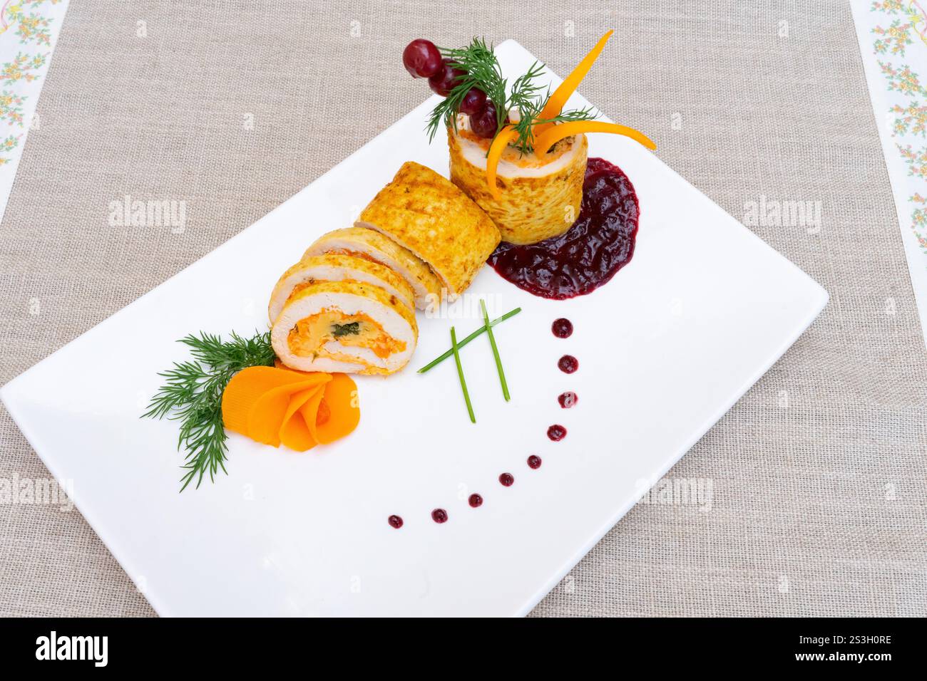 Un petit pain de poulet gastronomique magnifiquement plaqué composé de couches de viande et de légumes. Servi avec des garnitures vibrantes et une sauce riche, ce plat est idéal Banque D'Images