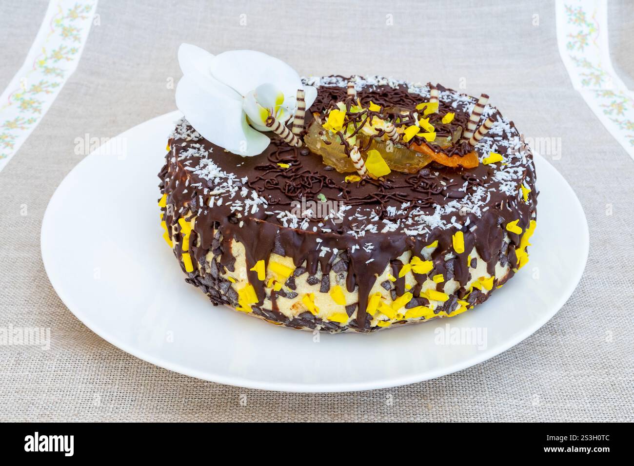 Un gâteau au chocolat magnifiquement conçu se trouve élégamment sur une assiette blanche, orné de vermicelles jaunes vives et de délicates fleurs comestibles, le mettant en valeur Banque D'Images