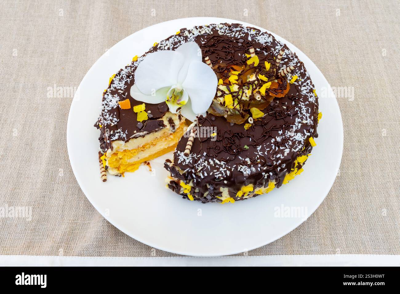 Un gâteau au chocolat magnifiquement conçu se trouve sur une assiette blanche. Une tranche a été enlevée, révélant des couches de crème et de fruits. Le gâteau est orné de Banque D'Images
