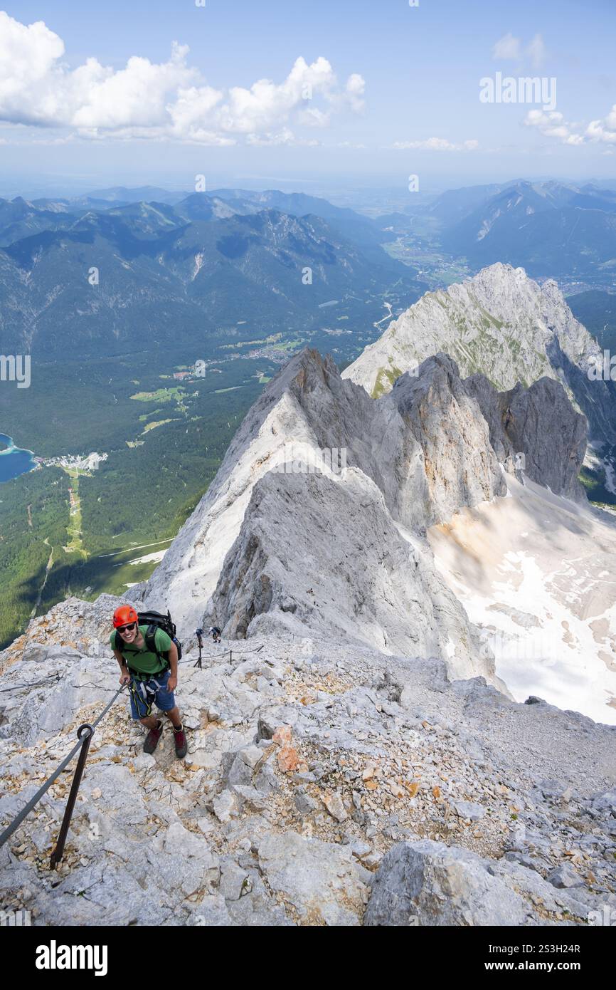 Alpiniste avec casque dans une via ferrata sécurisée, via ferrata Zugspitz, montée à la Zugspitze, vue sur la crête de montagne avec Waxenstein et Riffelspit Banque D'Images