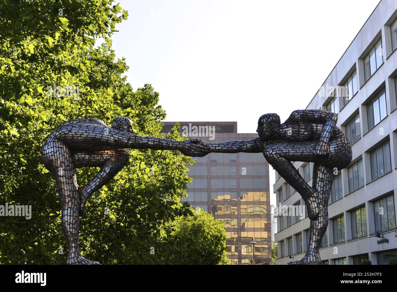 Deux sculptures en métal escamotées tenant la main, entourées de bâtiments urbains et d'arbres verts, Londres, région de Londres, Angleterre, Royaume-Uni, Europe Banque D'Images