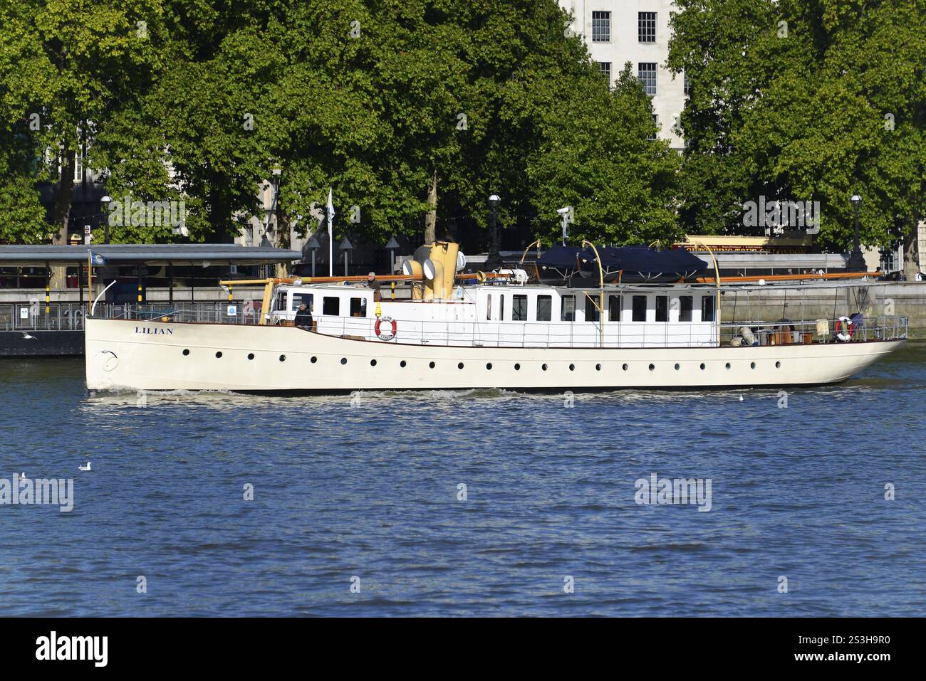 Un bateau blanc navigue le long de la rivière entouré d'arbres verts et de bâtiments urbains, Londres, région de Londres, Angleterre, Royaume-Uni, Europe Banque D'Images
