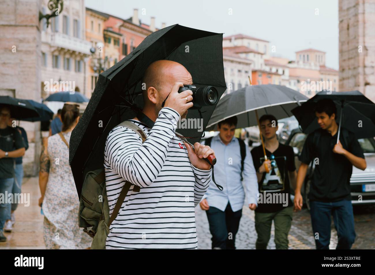 Un homme prend des photos et explore la ville un jour de pluie dans une rue bondée. Le photographe est avec le parapluie. Vérone, Italie - 06 juillet 2024 Banque D'Images