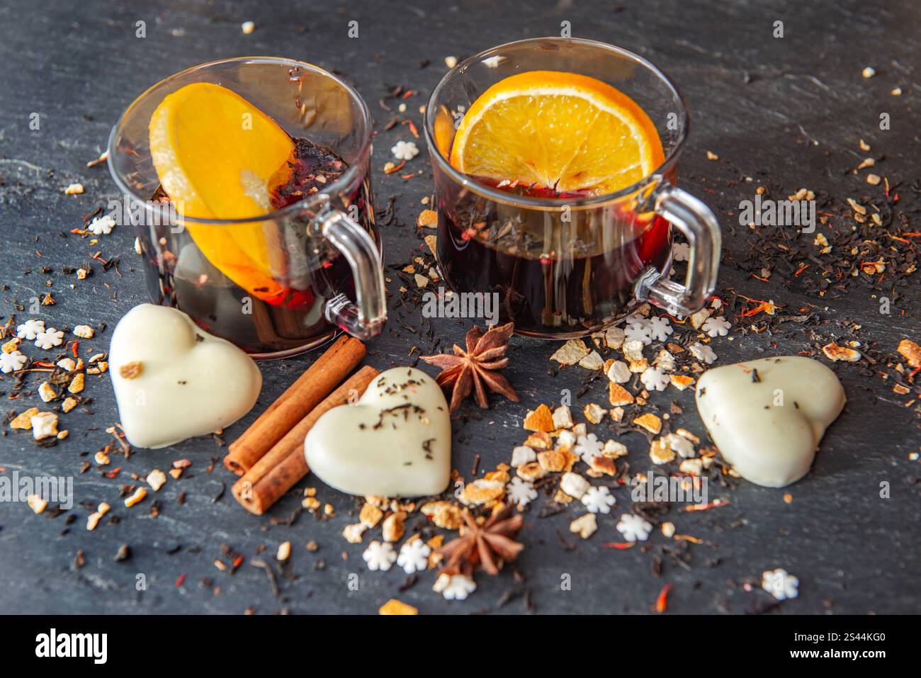 tranche d'orange dans du vin chaud dans deux verres avec des biscuits en forme de coeur et des épices disposés sur un fond d'ardoise grise Banque D'Images
