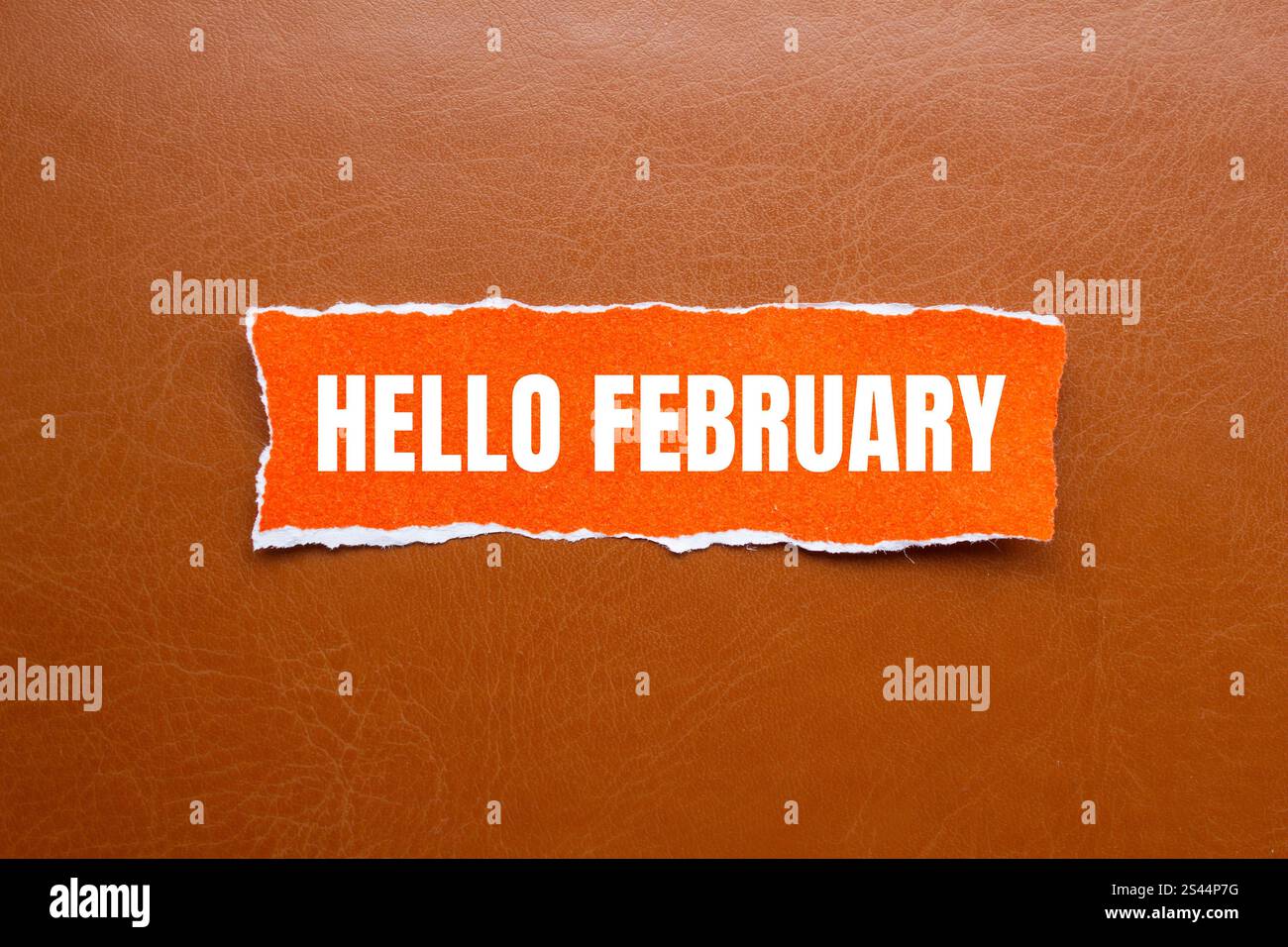 Bonjour février message écrit sur un morceau de papier déchiré orange déchiré avec fond brun. Symbole conceptuel bonjour février. Copier l'espace. Banque D'Images