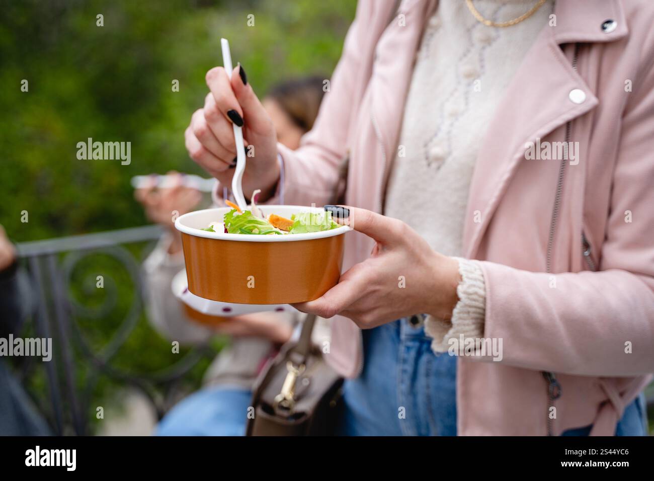 Gros plan des mains d’une femme tenant un bol sans plastique avec une salade fraîche à l’extérieur. L'image met en évidence une alimentation durable, saine et écologique Banque D'Images