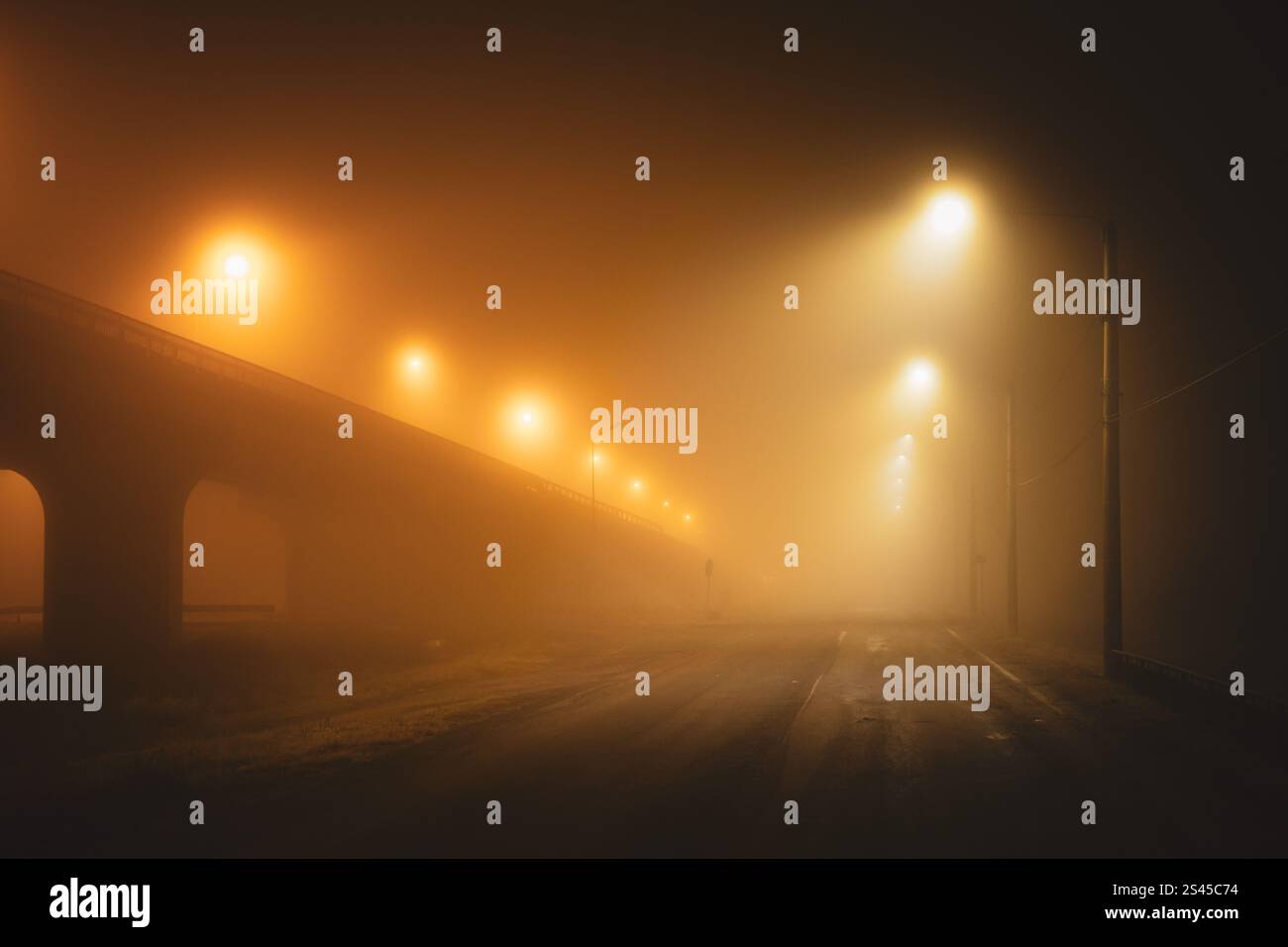 Lumières de rue orange Moody illuminant une route urbaine vide par une nuit d'hiver brumeuse. Pas de voitures, pas de gens Banque D'Images