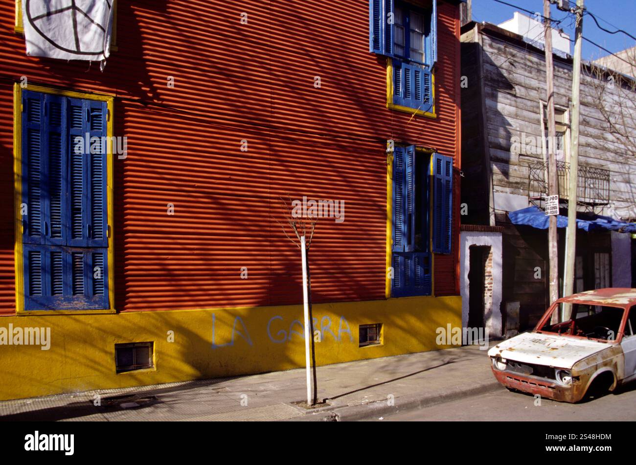 Scène de rue animée à la Boca, Buenos Aires, Argentine, avec des bâtiments colorés et une voiture abandonnée. Banque D'Images