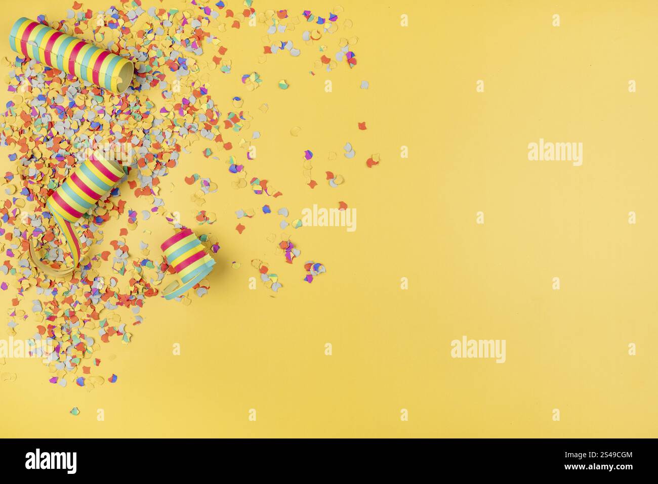 Confettis colorés et banderoles en papier dispersés sur un fond jaune, carnaval Banque D'Images