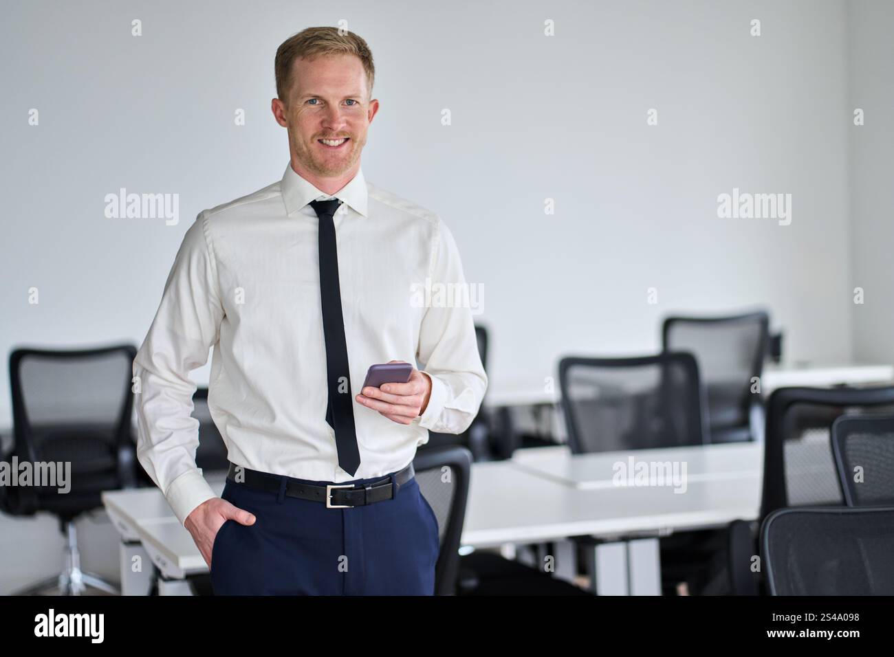 Heureux jeune homme d'affaires confiant utilisant smartphone dans le bureau. Portrait. Banque D'Images