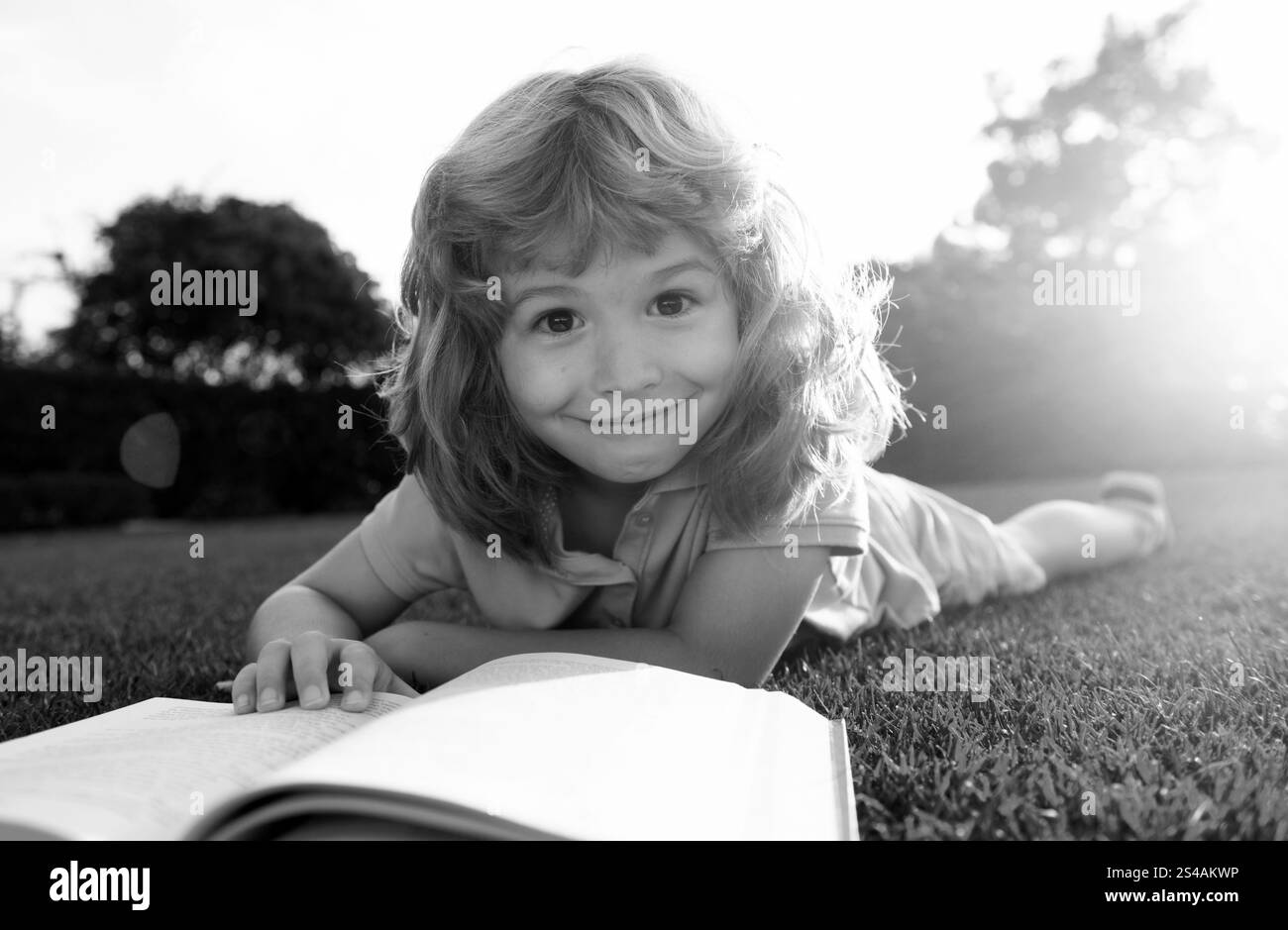 Mignon garçon lisant un livre sur l'herbe. Un enfant lit un livre dans le parc d'été. Banque D'Images
