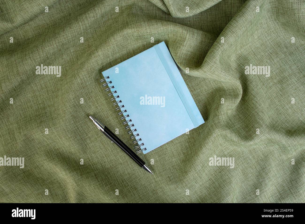 Cahier à couverture rigide bleu vide avec un stylo à bille sur fond de tissu vert olive, espace de copie pour le texte Banque D'Images
