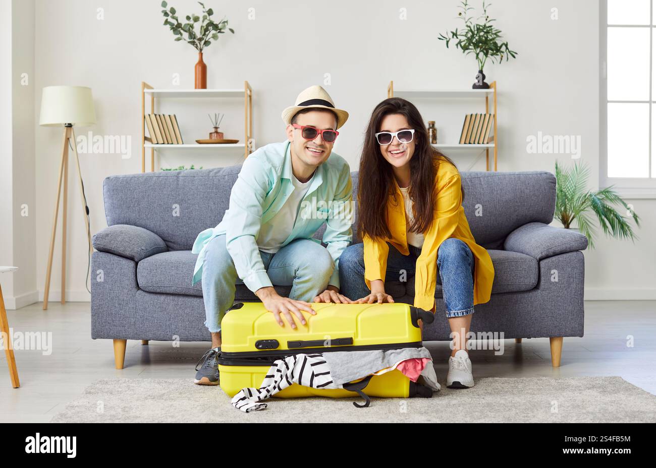 Jeune couple positif emballant leur valise, se préparant pour le voyage de vacances et regardant la caméra. Banque D'Images