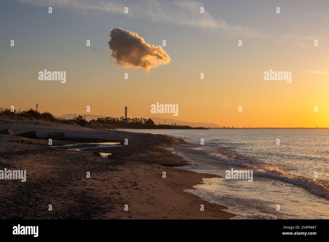 Plage de sable illuminée par la lumière du soleil d'un coucher de soleil tôt. Petites vagues de la mer Tyrrhénienne (Méditerranée). Ciel bleu avec un nuage éclairé. Spadafora, SiC Banque D'Images