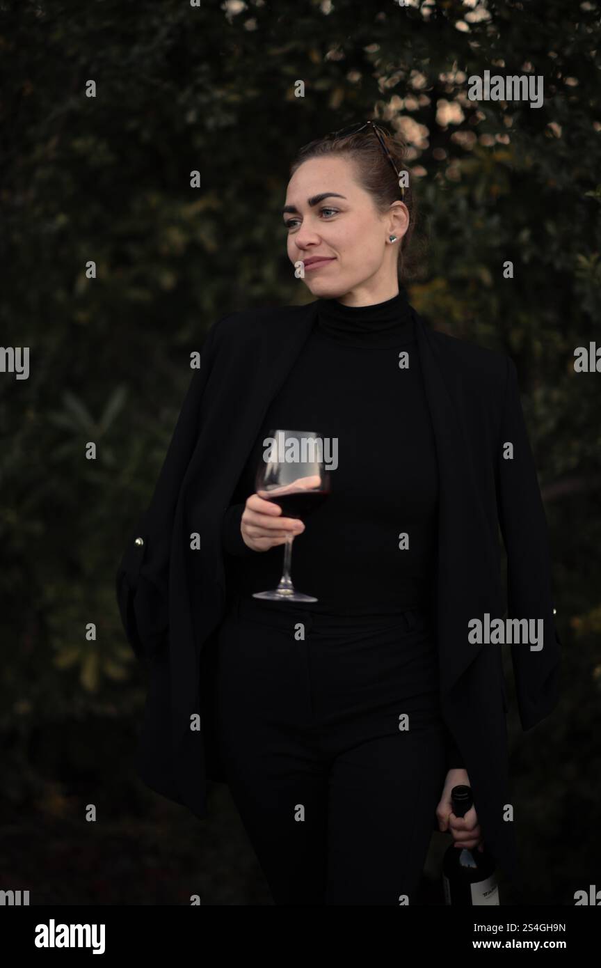 Fille avec un verre de vigne sur une partie sur la cour arrière en costume noir Banque D'Images