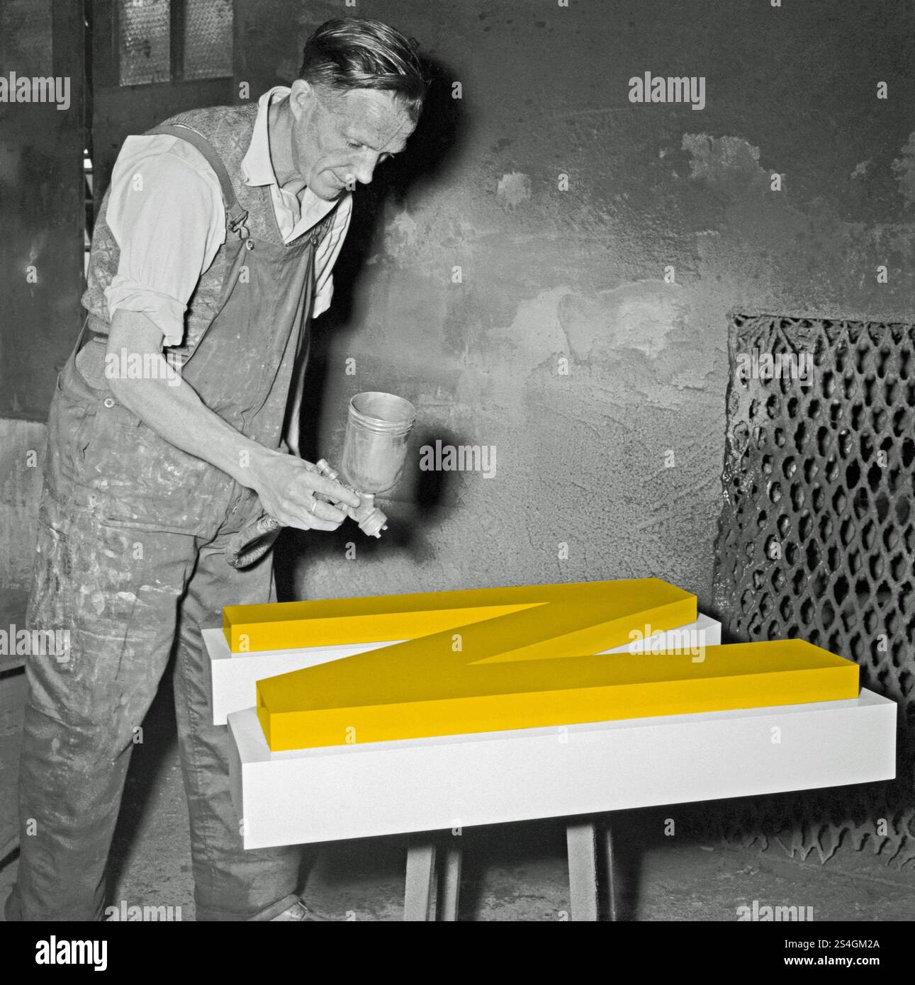 Un ouvrier peignant au pistolet une grande lettre en métal «N» dans un atelier de fonderie britannique vers 1930. Cette photographie vintage en noir et blanc a été améliorée numériquement pour que la lettre soit de couleur jaune. Banque D'Images Un ouvrier peignant au pistolet une grande lettre en métal «N» dans un atelier de fonderie britannique vers 1930. Cette photographie vintage en noir et blanc a été améliorée numériquement pour que la lettre soit de couleur jaune. Banque D'Images
