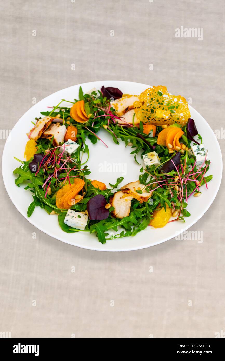 Une salade circulaire est artistiquement arrangée avec des légumes verts mélangés, du poulet grillé et des légumes colorés. La présentation vibrante met en valeur Fresh ingre Banque D'Images