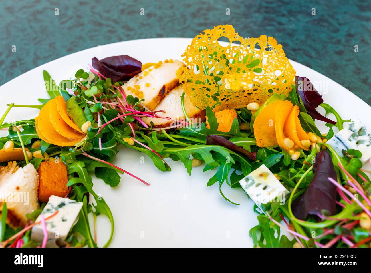 Une salade gastronomique colorée se compose de légumes verts mélangés, de tranches de poulet, de légumes vifs et de garnitures. Le plat présente un mélange de textures et de saveurs, Banque D'Images
