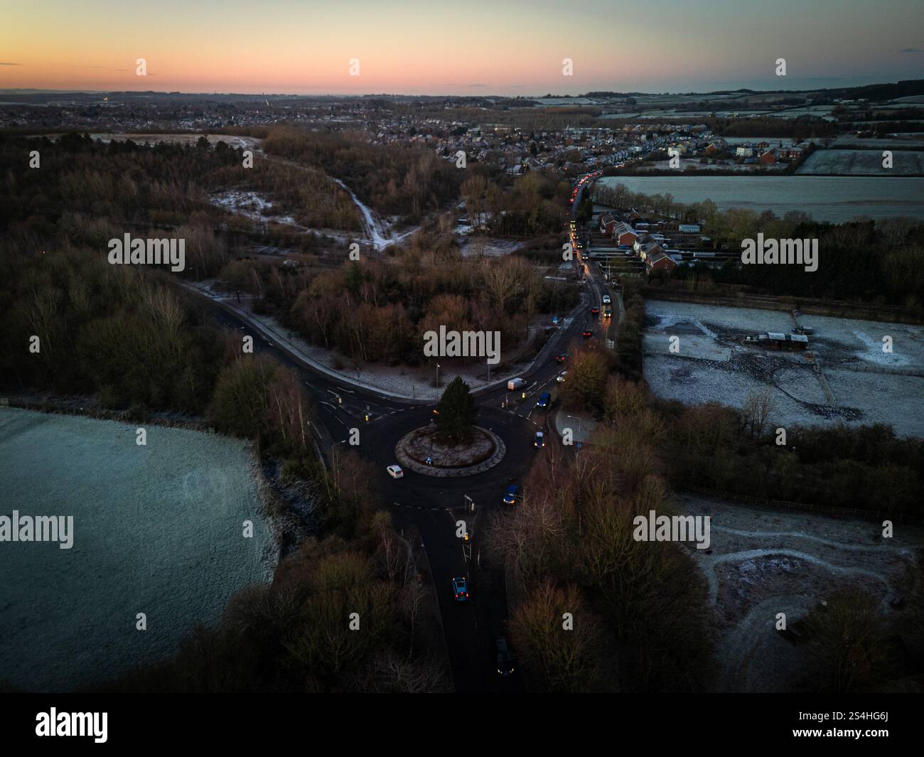 Vue aérienne de voitures circulant sur un rond-point à l'aube près d'un village en hiver Banque D'Images