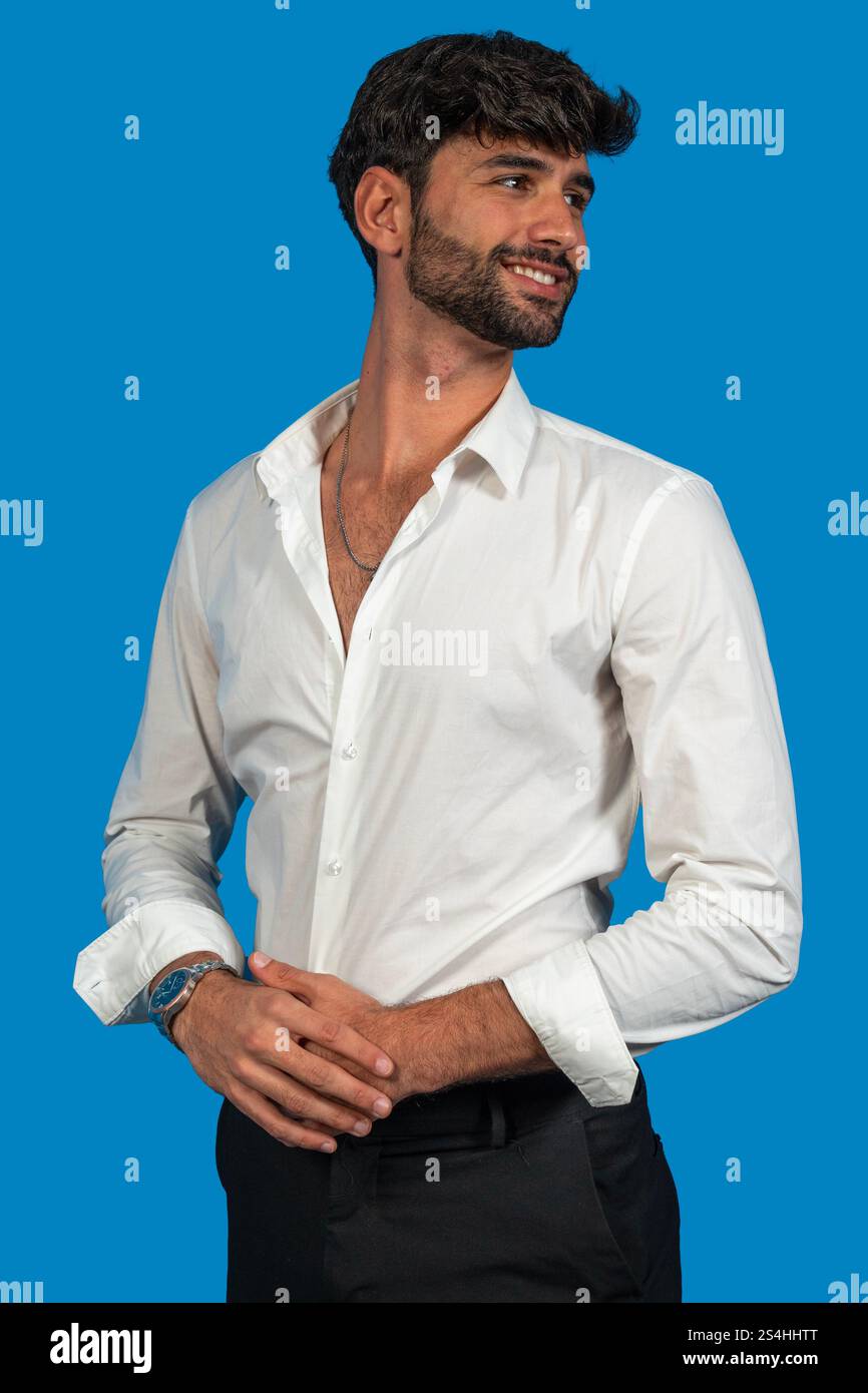 Jeune homme d'affaires portant chemise blanche et montre-bracelet, souriant et regardant loin sur fond bleu Banque D'Images