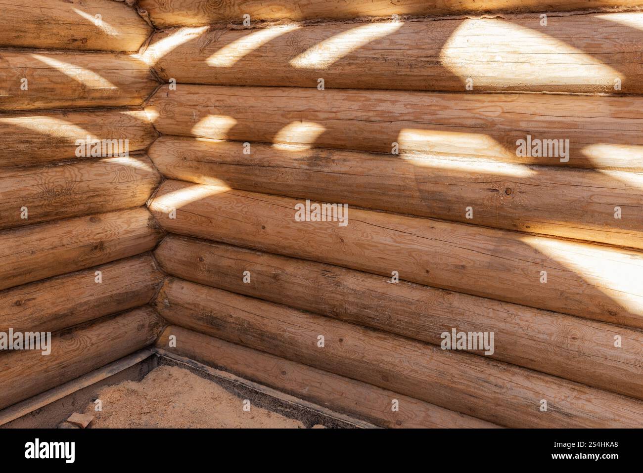 Un coin intérieur d'un nouvel intérieur de maison en bois fait de bûches de pin naturel non coloré avec des faisceaux lumineux sur les murs, photo de fond. La maison en rondins est unde Banque D'Images