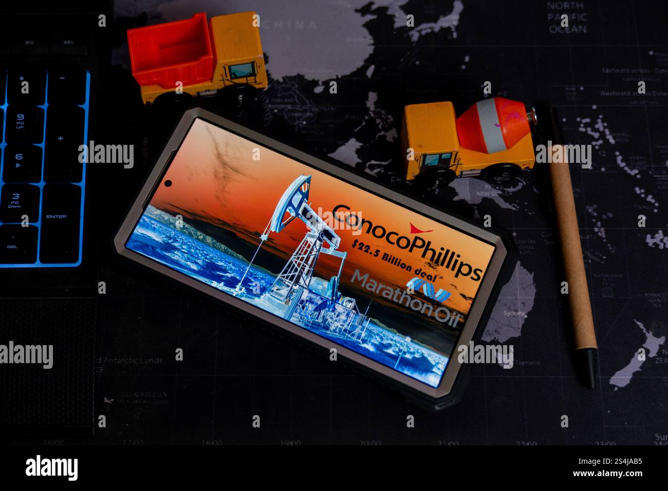 Smartphone affichant l'acquisition de Marathon Oil par ConocoPhillips, positionnée sur une carte du monde, aux côtés de camions jouets et d'un stylo, symbolisant ener mondial Banque D'Images