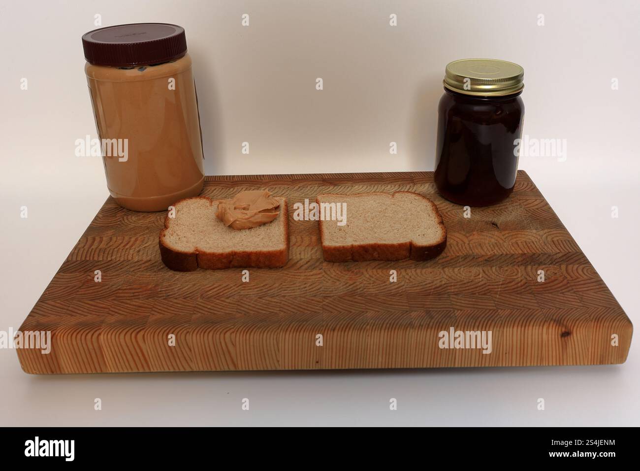 Sandwich au beurre d'arachide et à la gelée, étant fait sur une planche à découper devant un fond blanc Banque D'Images Sandwich au beurre d'arachide et à la gelée, étant fait sur une planche à découper devant un fond blanc Banque D'Images