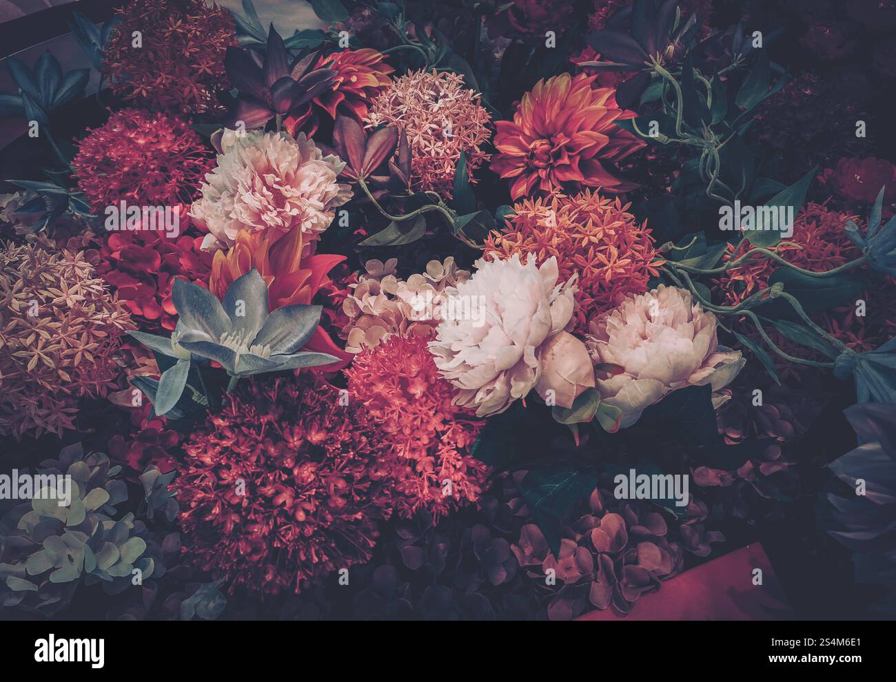 Une image de style vintage mettant en valeur un arrangement luxuriant de fleurs artificielles, principalement dans des rouges et roses profonds. La composition suggère une célébration Banque D'Images