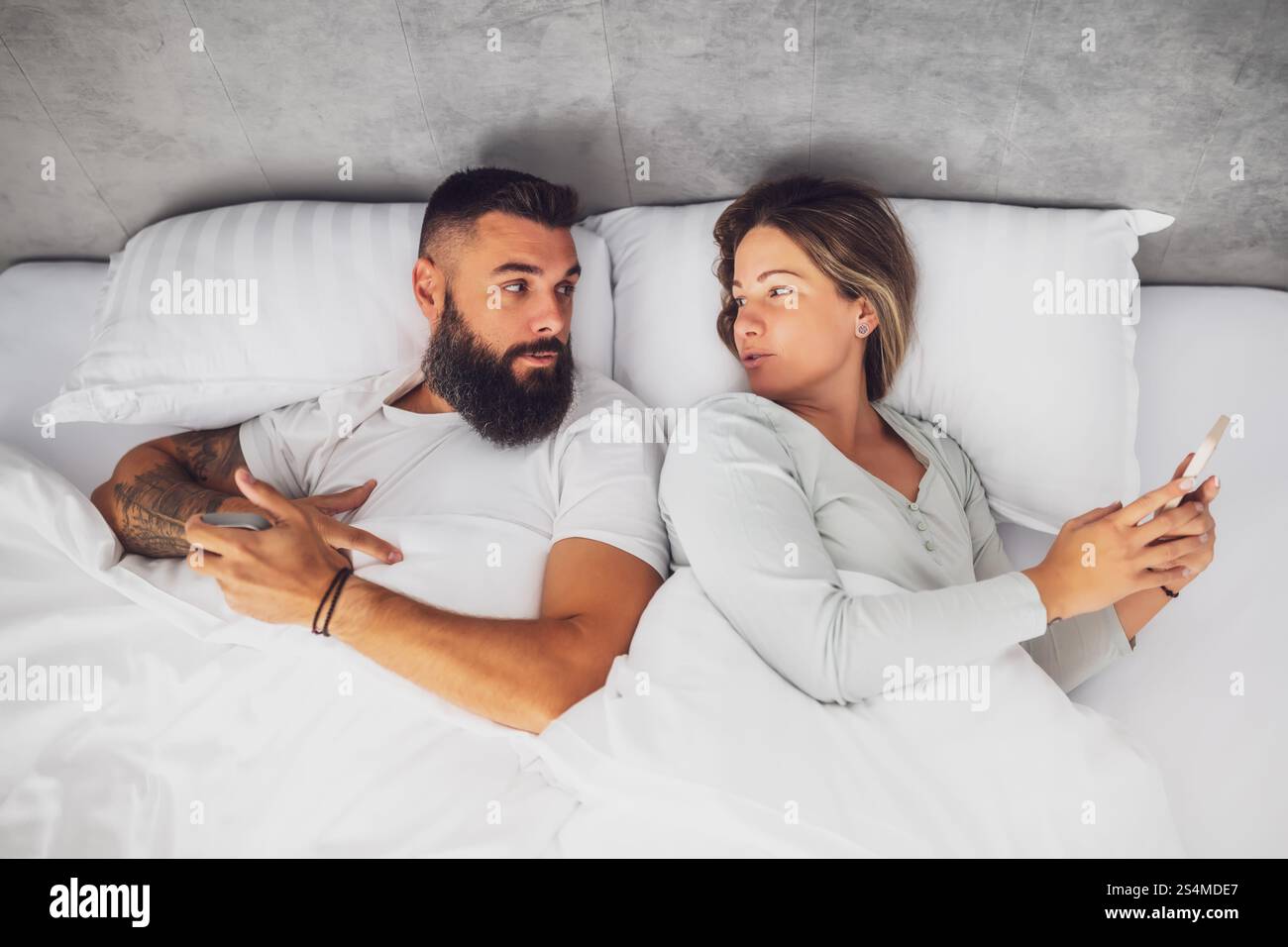 Jeune couple heureux est couché dans le lit le matin. Ils utilisent des smartphones. Banque D'Images