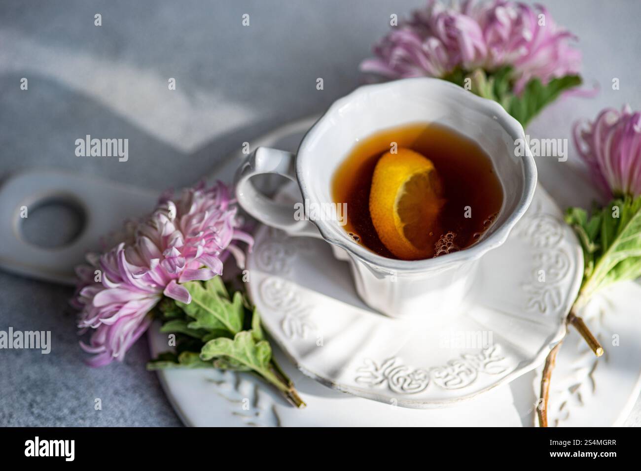 Élégante configuration sur le thème de l'automne avec une boisson chaude avec une tranche de citron dans une tasse blanche entourée de chrysanthèmes roses délicats sur une surface rustique Banque D'Images