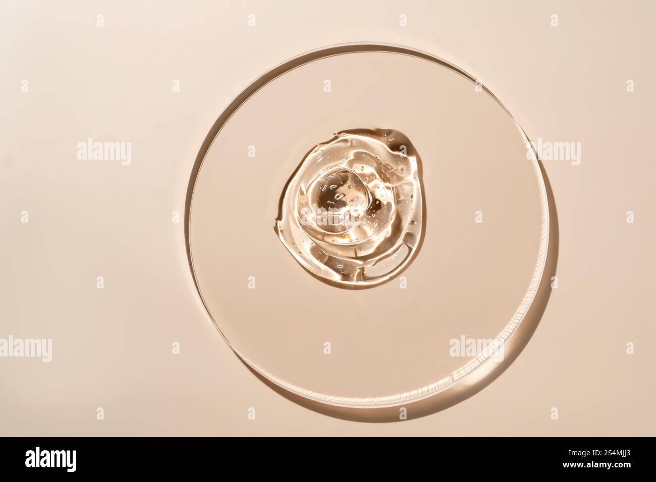Une vue en grand angle d'une gouttelette de sérum transparente sur une surface en verre lisse, éclairée par une lumière chaude, l'image met en évidence la texture et la clarté dans un minimali Banque D'Images