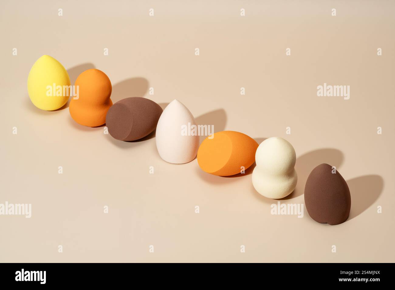 Une rangée d'éponges cosmétiques dans des tons vibrants de jaune, orange et brun affichés sur un fond neutre idéal pour l'application de maquillage, le mélange, et Banque D'Images