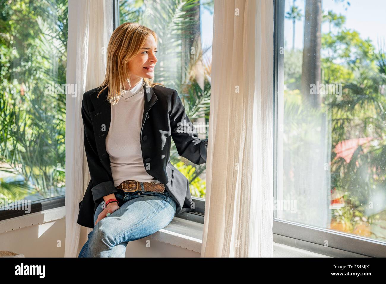 Femme assise près d'une grande fenêtre dans un bureau à domicile moderne, regarder la lumière du soleil à l'extérieur inonde la pièce, créant une atmosphère sereine et productive pour à distance Banque D'Images